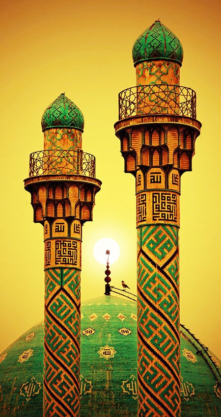 Two intricately designed minarets with Arabic calligraphy against a glowing sunset.