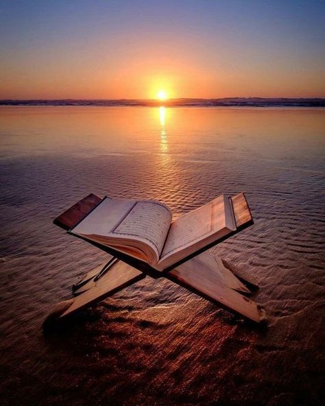 Open Quran placed on a wooden stand on the beach during sunset